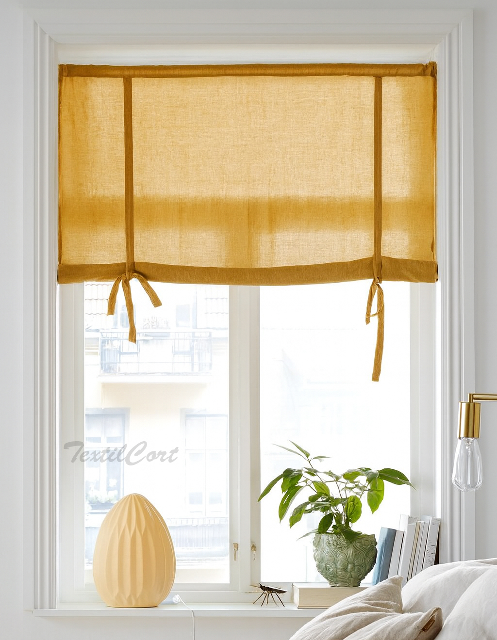 Estor con lazos en color mostaza Estor con lazos decorativos en tejido mostaza translúcido sobre ventana blanca en dormitorio luminoso de estilo nórdico